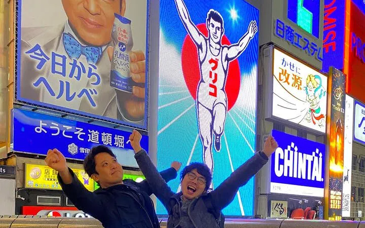 Dotonbori Glico sign with two people posing in front, Osaka street food tour.