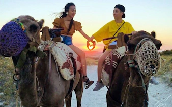 Cappadocia camel ride at sunrise with hot air balloons in the background.