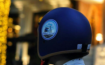 Vespa helmet with Hanoi Local Vespa Tours logo, evening street lights in Hanoi.