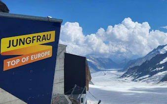 Jungfraujoch sign with view of Aletsch Glacier under cloudy sky, Switzerland.