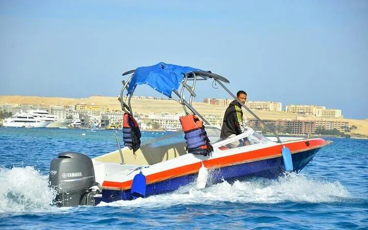 Speedboat on clear water heading to Hula Hula Island, Hurghada, with cityscape in the background.