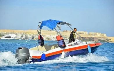 Speedboat on clear water heading to Hula Hula Island, Hurghada, with cityscape in the background.