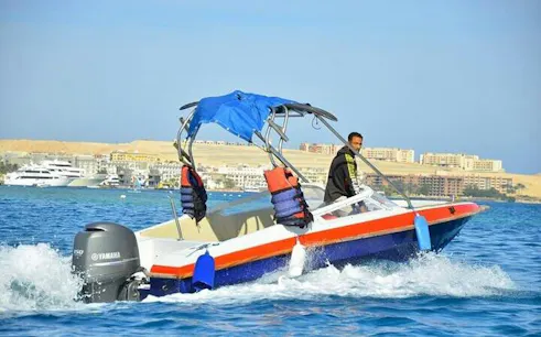 Speedboat on clear water heading to Hula Hula Island, Hurghada, with cityscape in the background.