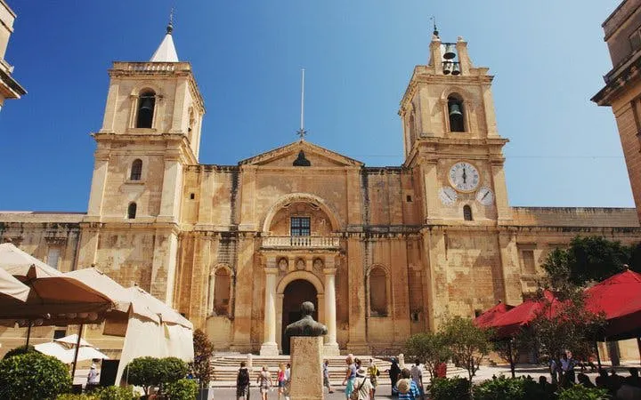 St. John's Co-Cathedral facade in Valletta, Malta, with tourists exploring the square.