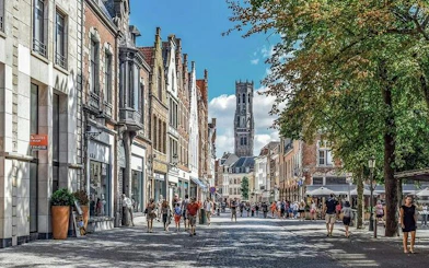 Street view in Bruges with Belfry tower in the background, tourists walking and exploring.