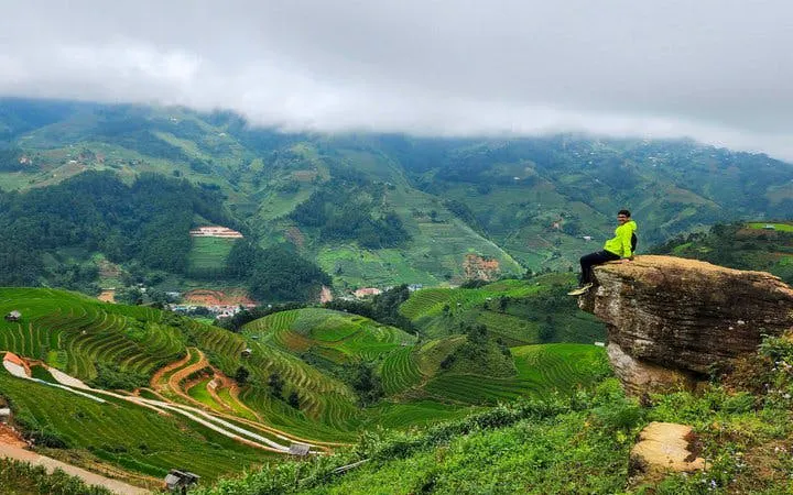 Mu Cang Chai terraced fields with person sitting on rock ledge, Vietnam.