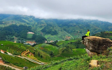 Mu Cang Chai terraced fields with person sitting on rock ledge, Vietnam.