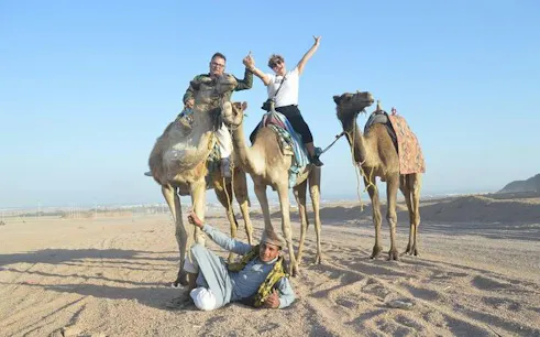Camel ride adventure in Sharm El Sheikh with two tourists on camels and a guide in the desert.