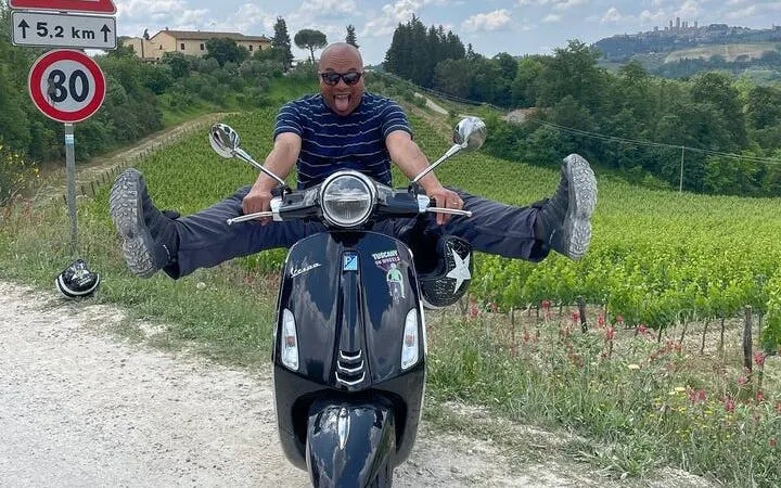 Man enjoying Vespa ride through Chianti vineyards on private tour with Tuscan lunch and wine tasting.
