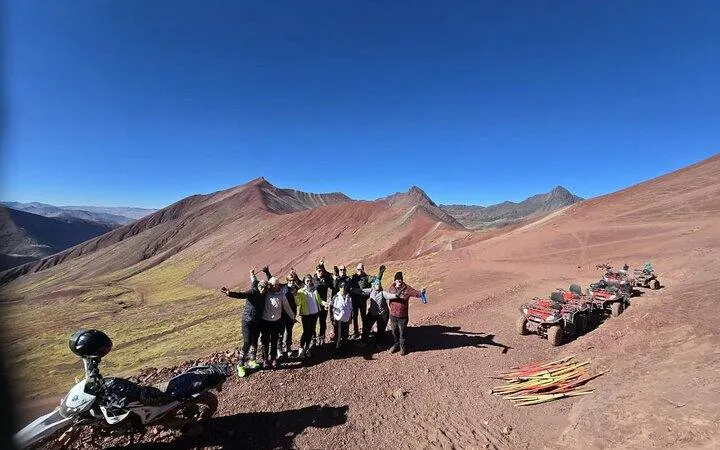 Group of tourists on Rainbow Mountain ATV tour with red terrain and ATVs, Cusco.