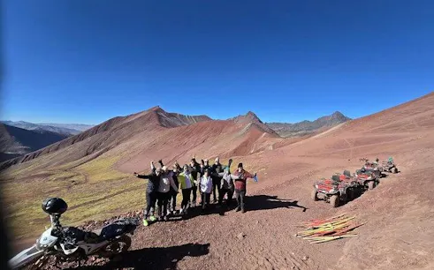 Group of tourists on Rainbow Mountain ATV tour with red terrain and ATVs, Cusco.