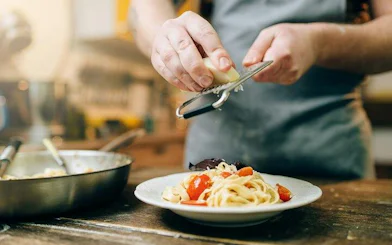 Person grating cheese over pasta during a sauce-making class in Rome.
