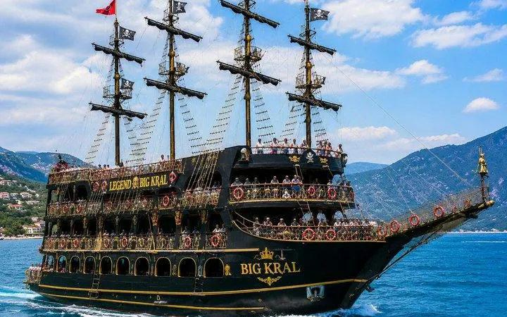 Pirate-themed boat with multiple decks on Alanya's blue waters, offering free drinks.