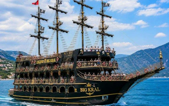 Pirate-themed boat with multiple decks on Alanya's blue waters, offering free drinks.