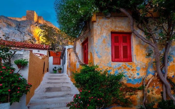 Stone steps and colorful houses in Plaka, Athens, with Acropolis in the background.