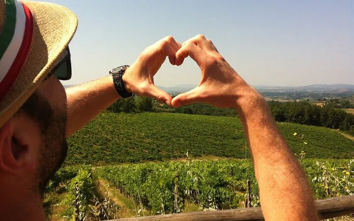 Hands forming a heart shape over a vineyard in Tuscany, Italy.