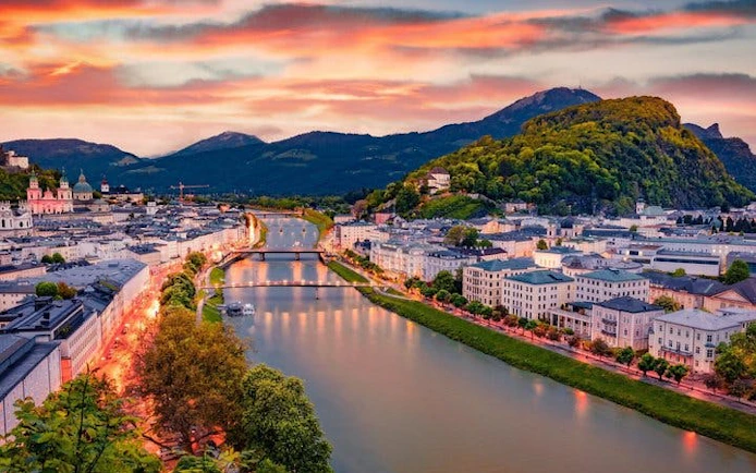 Salzburg cityscape with Salzach River and Hohensalzburg Fortress at sunset.