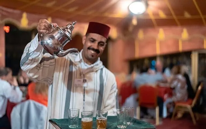 Server pouring traditional Moroccan tea at Chez-Ali dinner show in Marrakesh.