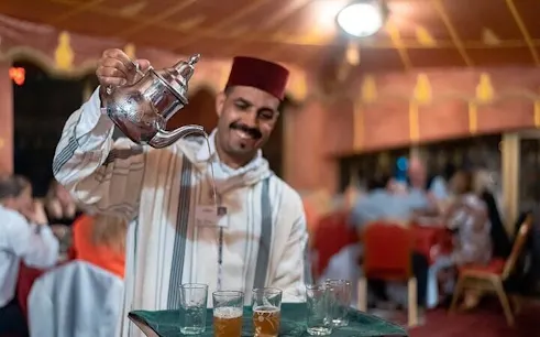 Server pouring traditional Moroccan tea at Chez-Ali dinner show in Marrakesh.