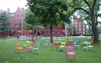 Harvard Yard with colorful chairs on the lawn, historic brick buildings in the background, Boston.