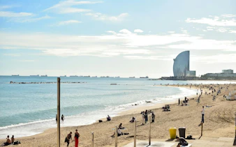 Barceloneta Beach with people relaxing, view of W Barcelona Hotel and ships in the distance.