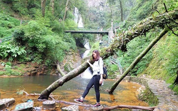 Woman exploring lush forest near waterfall on Sapa motorbike tour, Vietnam.