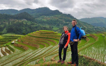 Two people standing on lush green rice terraces in Mu Cang Chai, Vietnam.