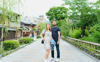 Couple walking in Kyoto's Gion district with traditional wooden buildings and greenery.