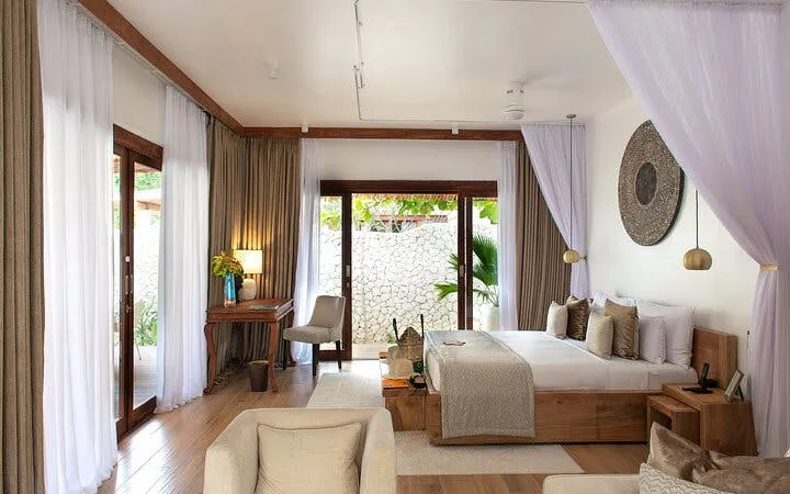 Luxurious Zanzibar hotel room with canopy bed, wooden decor, and garden view.