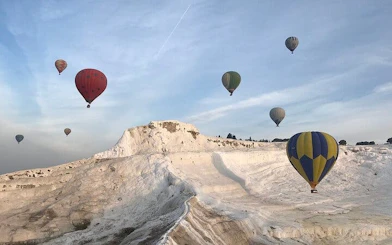 Hot air balloons over Pamukkale travertines and Hierapolis ruins in Turkey.