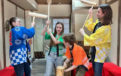 Group participating in traditional mochi pounding in Japan, wearing colorful costumes.