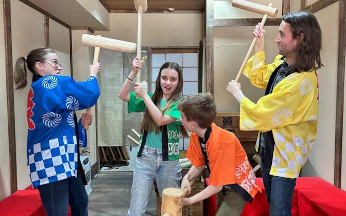 Group participating in traditional mochi pounding in Japan, wearing colorful costumes.