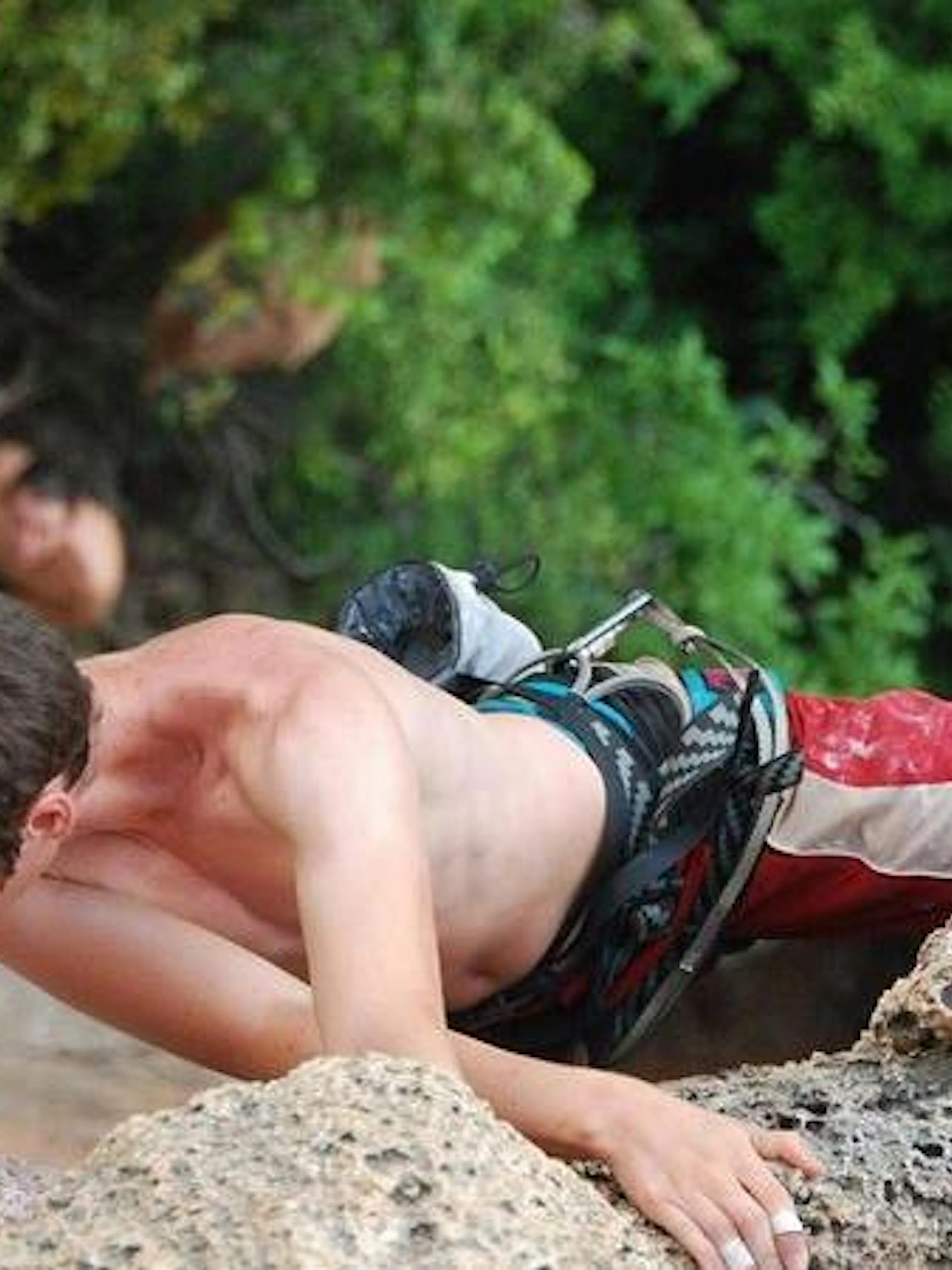 Rock climber ascending limestone cliff at Railay Beach, Krabi, with lush greenery in the background.