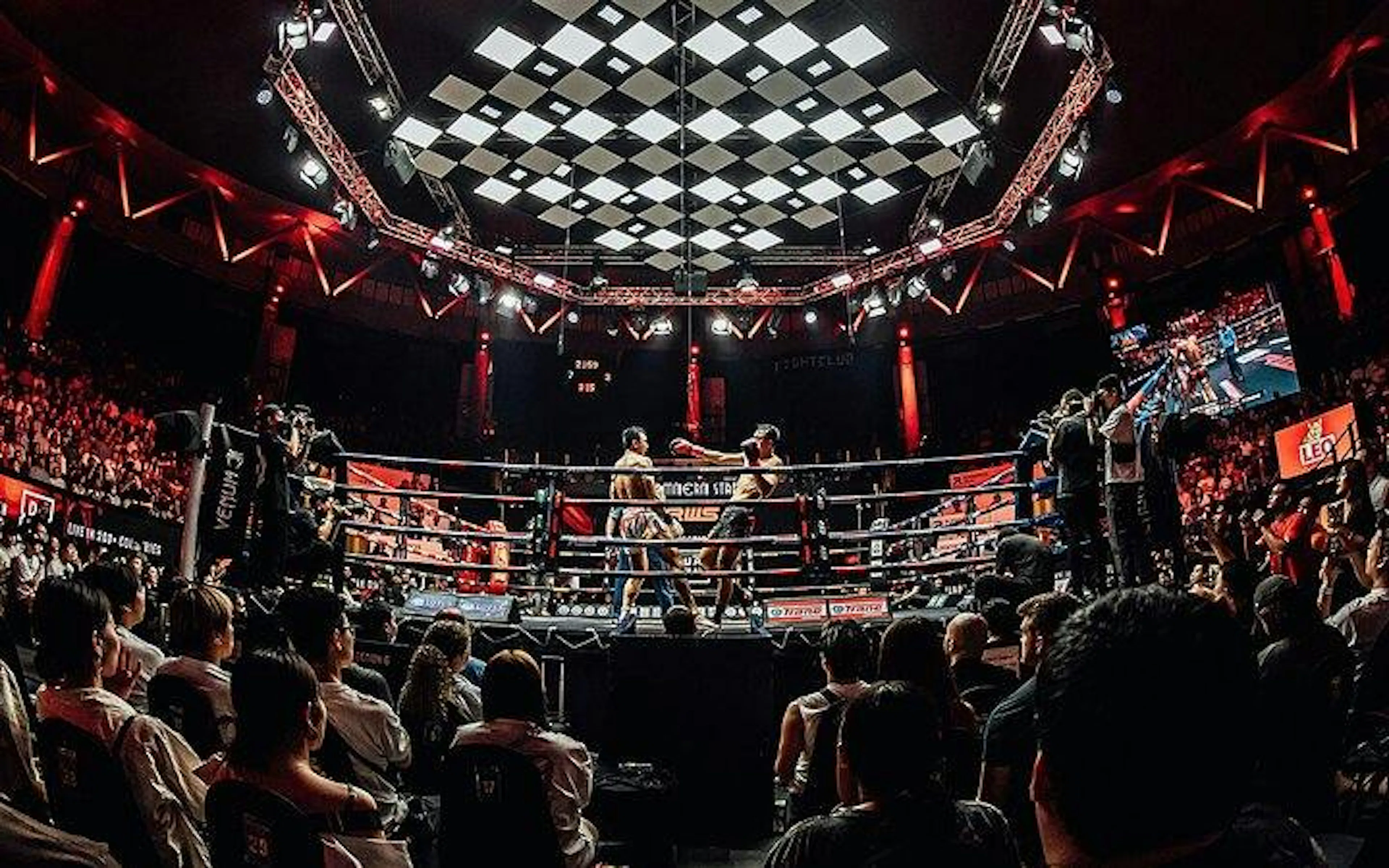 Muay Thai match at Rajadamnern Stadium, Bangkok with audience and photographers ringside.