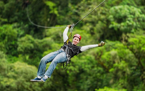 Person ziplining through lush forest at Waitomo Caves Zipline Park.