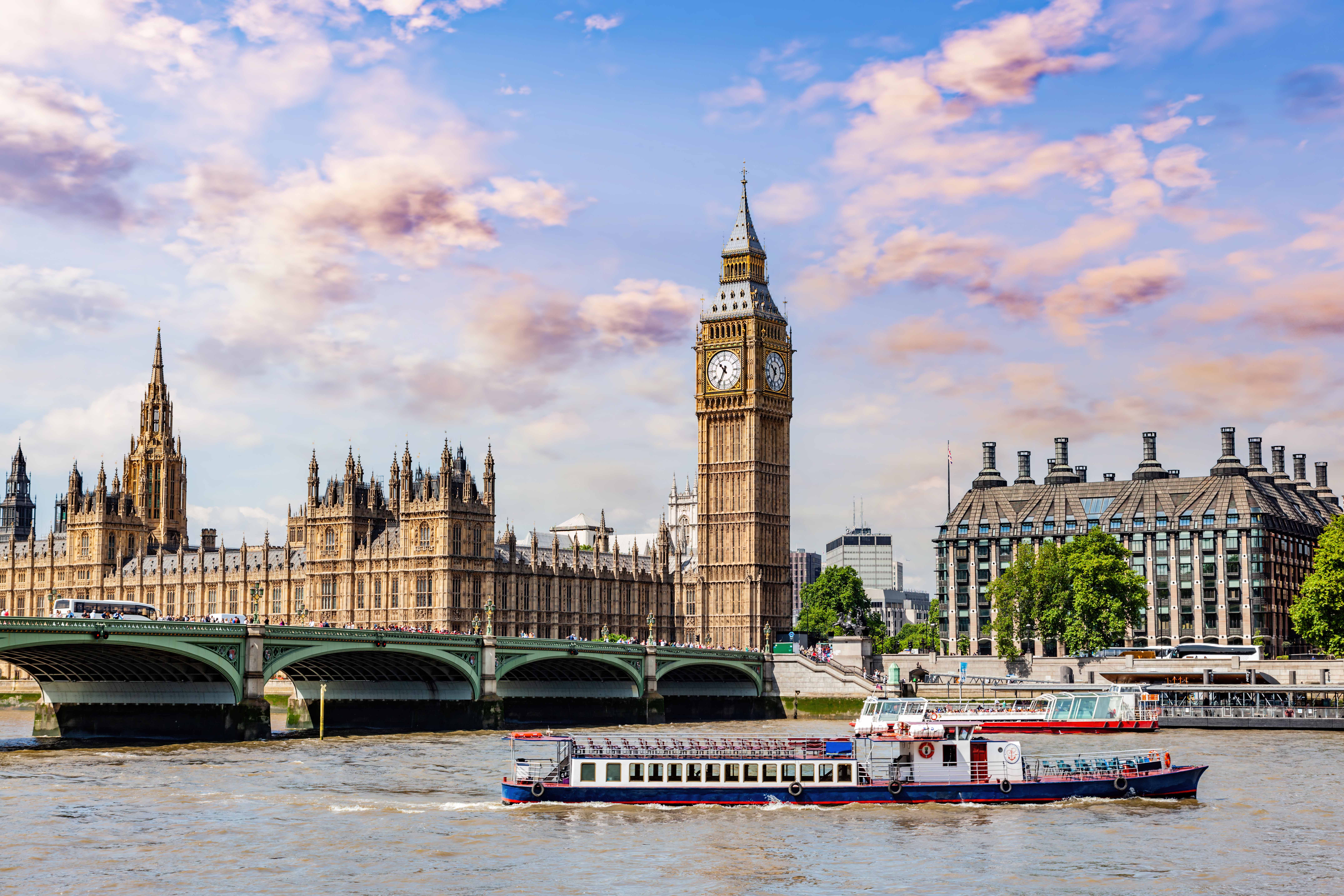 Thames River cruise boat passing by Big Ben and the Houses of Parliament in London.