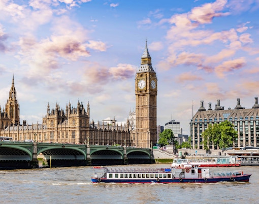 Thames River cruise boat passing by Big Ben and the Houses of Parliament in London.