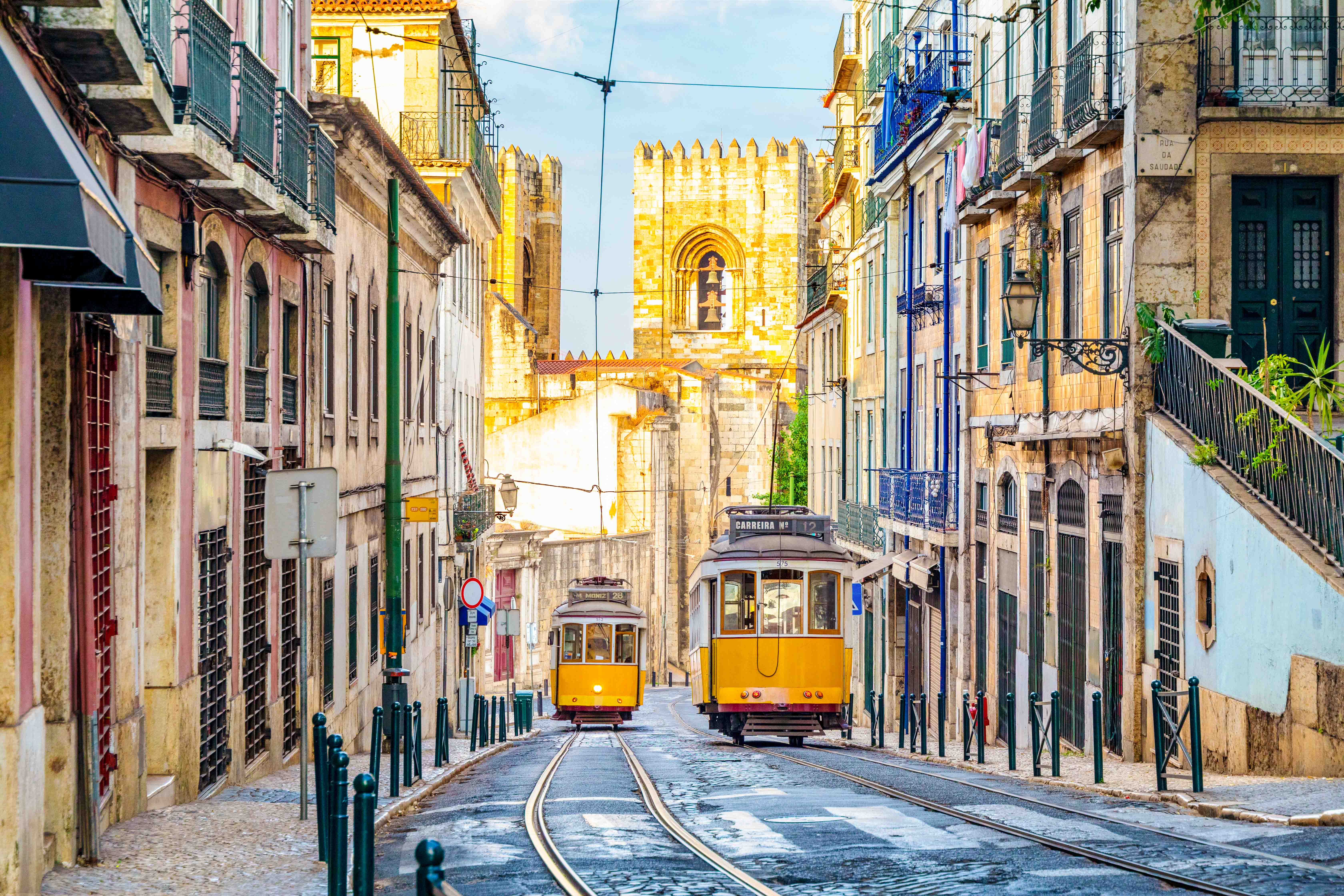 Lisbon trams on a narrow street with the Lisbon Cathedral in the background.