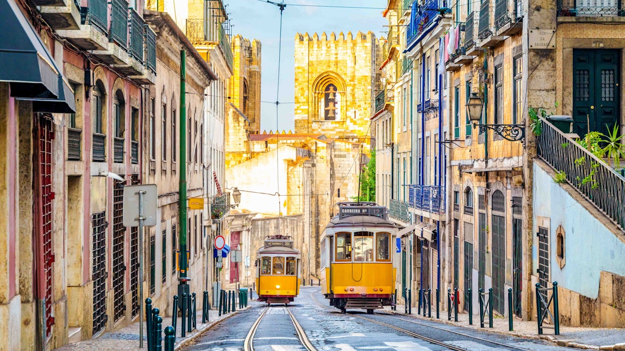 Lisbon trams on a narrow street with the Lisbon Cathedral in the background.
