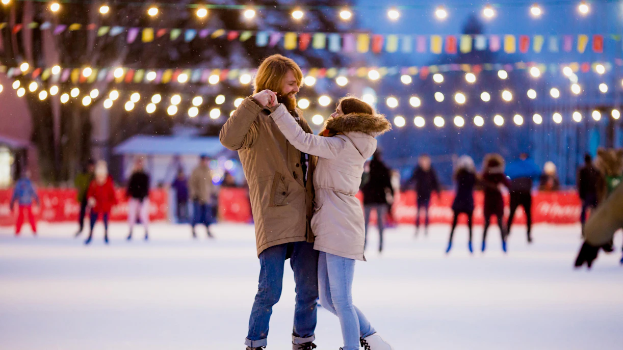 Couple ice skating under festive lights in Milan during Christmas.