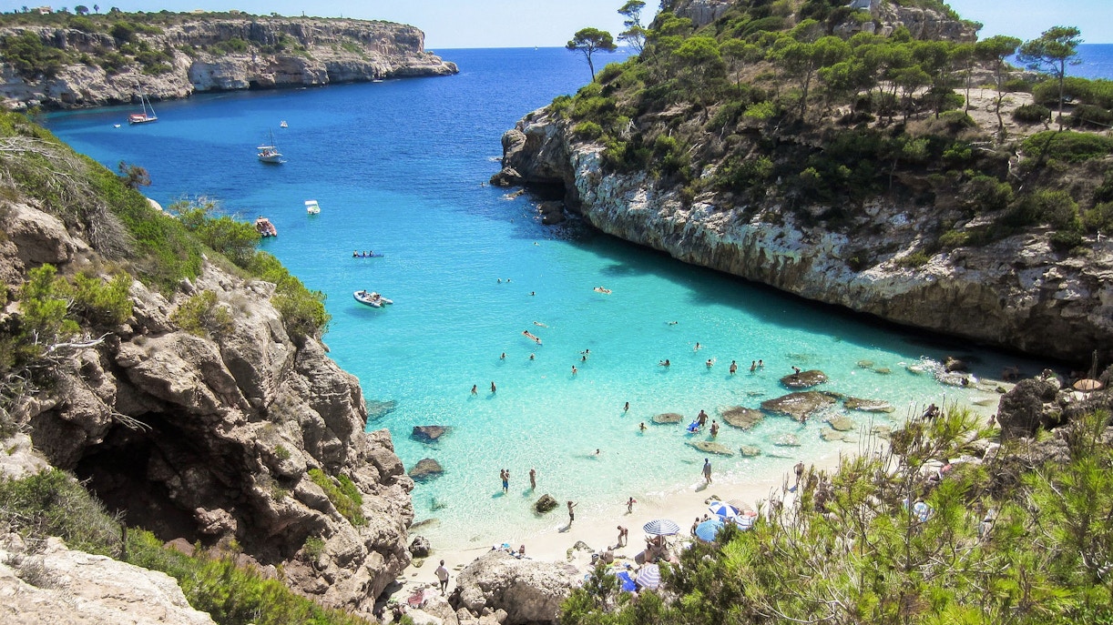 People swimming and relaxing on a scenic beach with clear blue water and rocky cliffs at Siloso Beach Walk, Singapore.