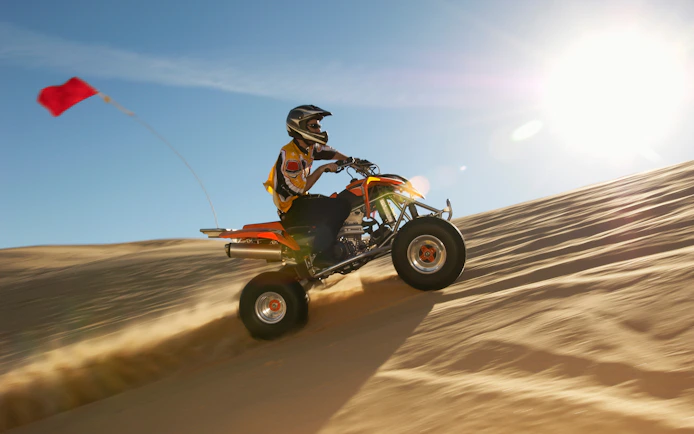 Quad biking on sand dunes in Dubai desert under bright sun.