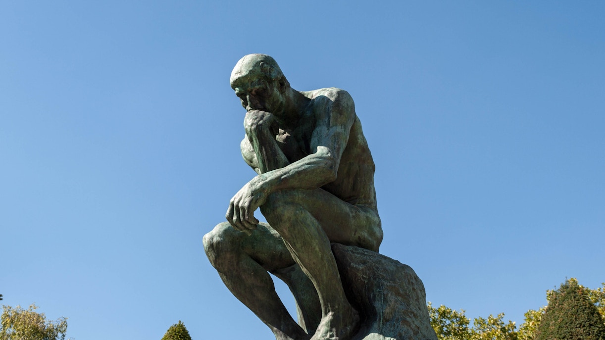 The Thinker sculpture in Rodin Museum gardens, Paris, surrounded by lush greenery.