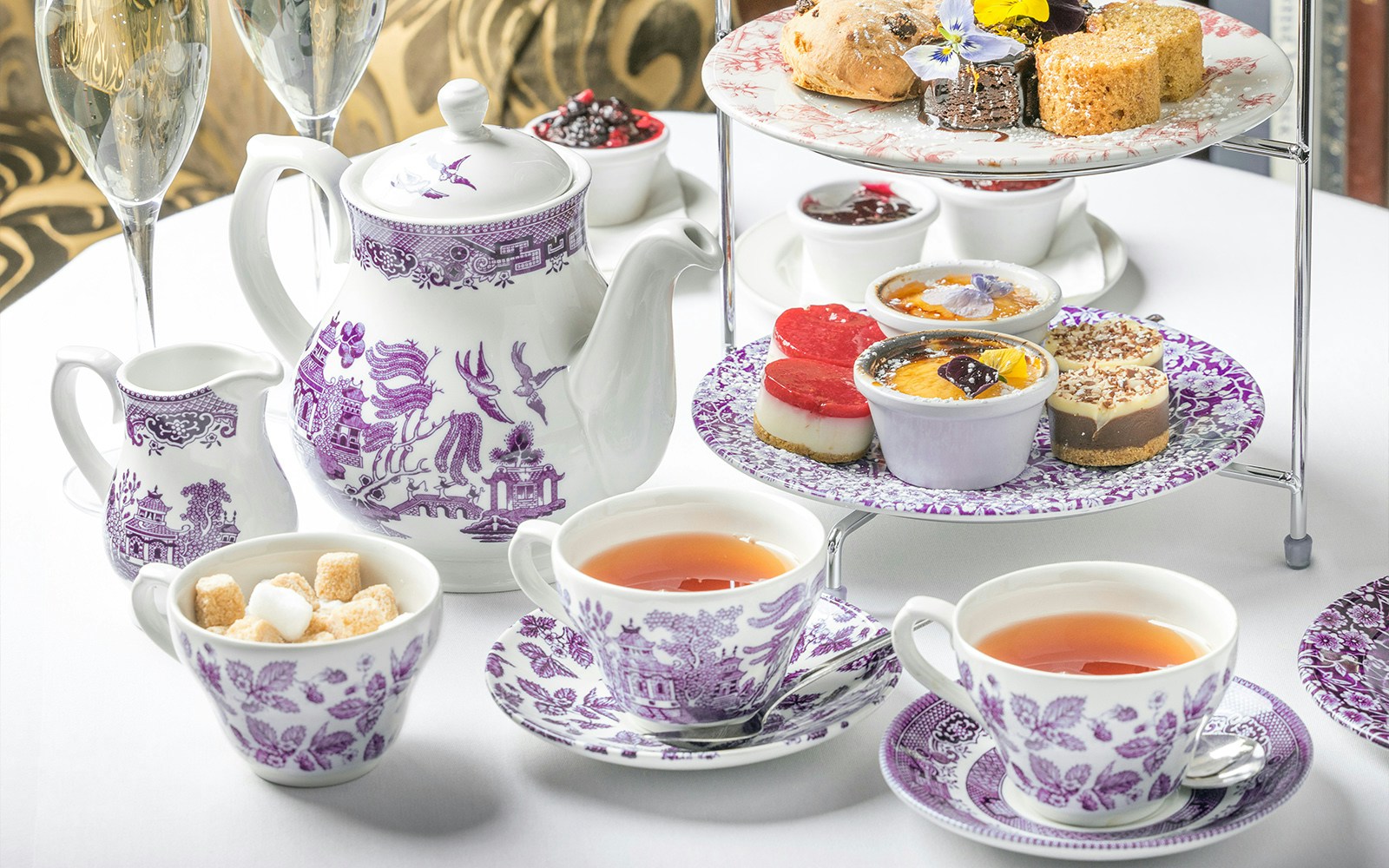 High tea setup with teapot, cups, and pastries on a table in a refined setting.