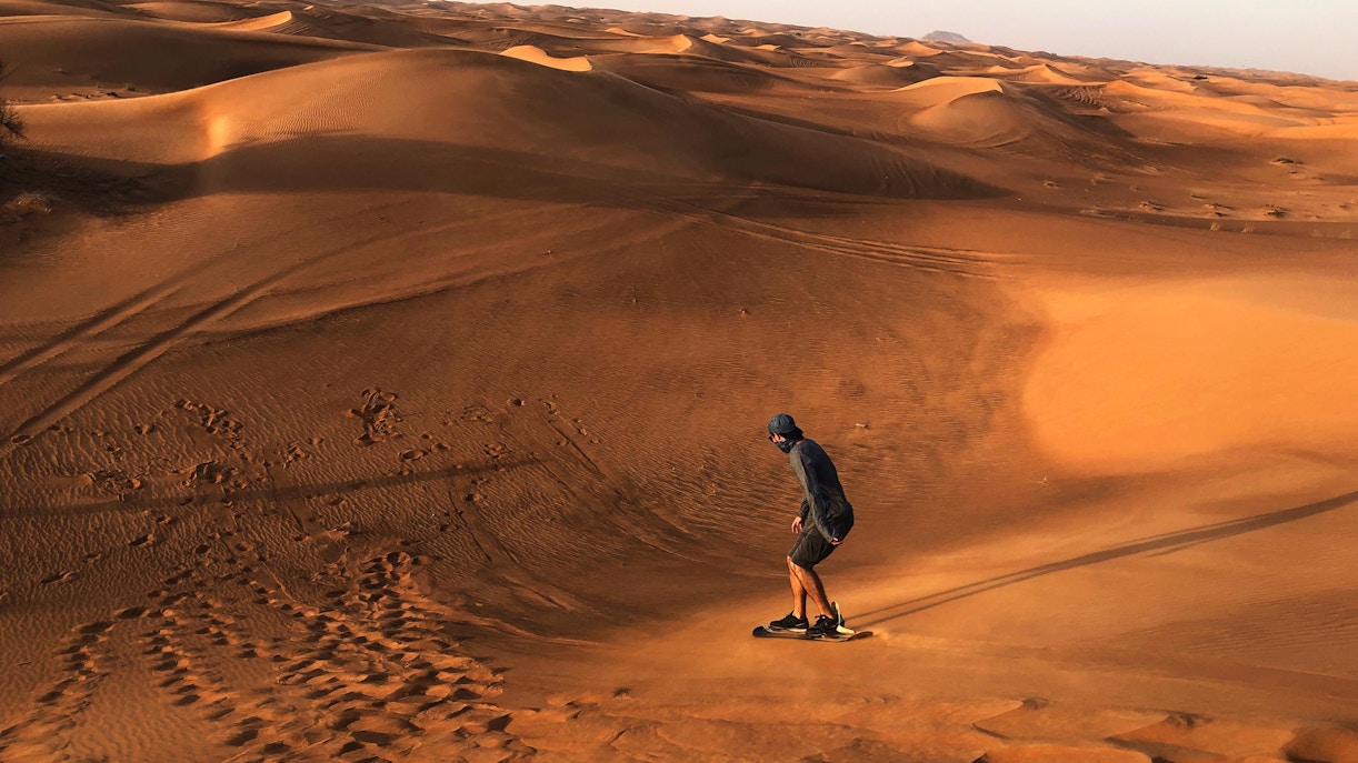 A boy sandboarding in the desert