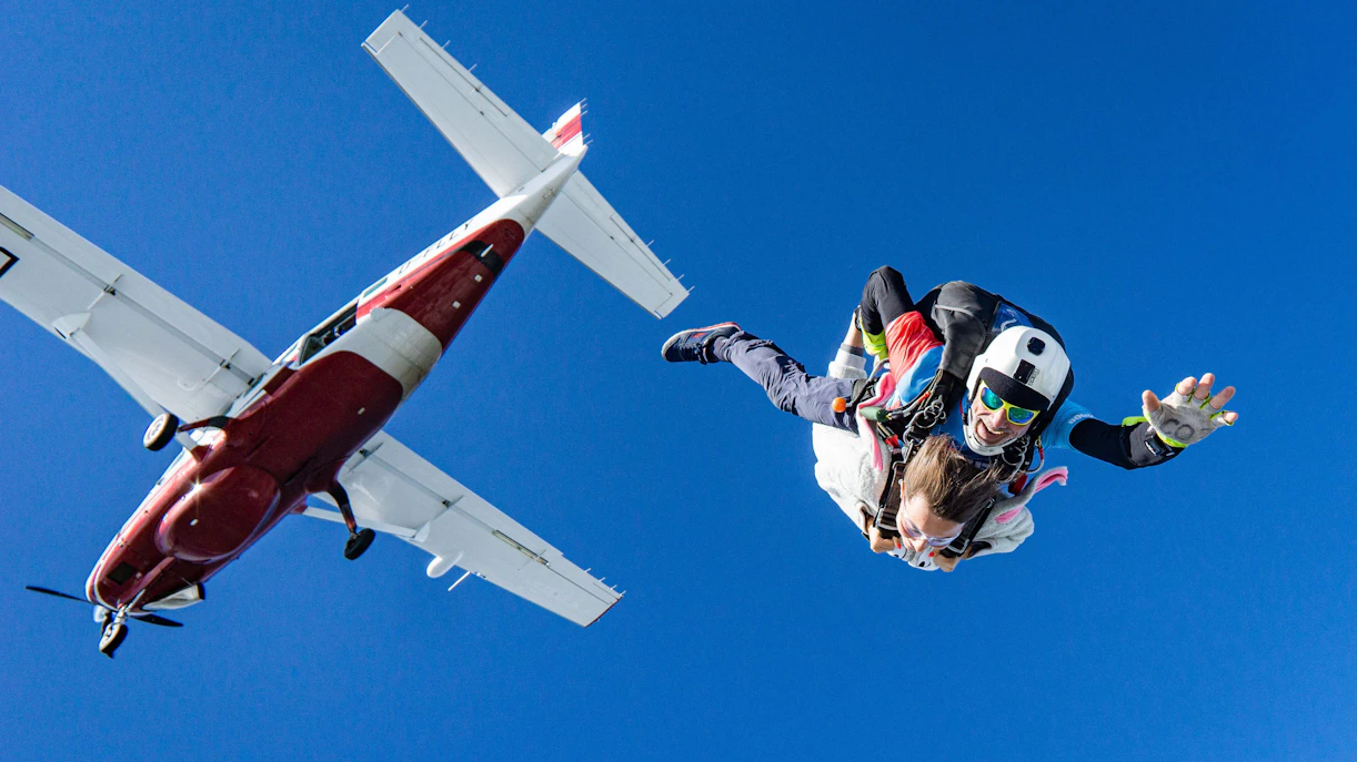 Tandem skydivers freefalling from a plane with clear blue sky.