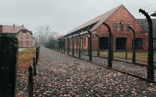 Barbed wire fence and brick buildings at Auschwitz-Birkenau State Museum.
