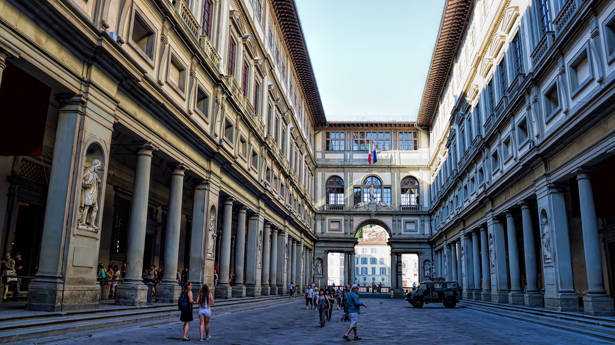Tourists wander through the spacious Uffizi Gallery courtyard, lined with statues and arches, a quiet prelude to the art treasures within