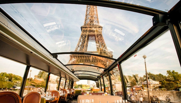 Seine River cruise with passengers dining at tables, Eiffel Tower architecture in the background.