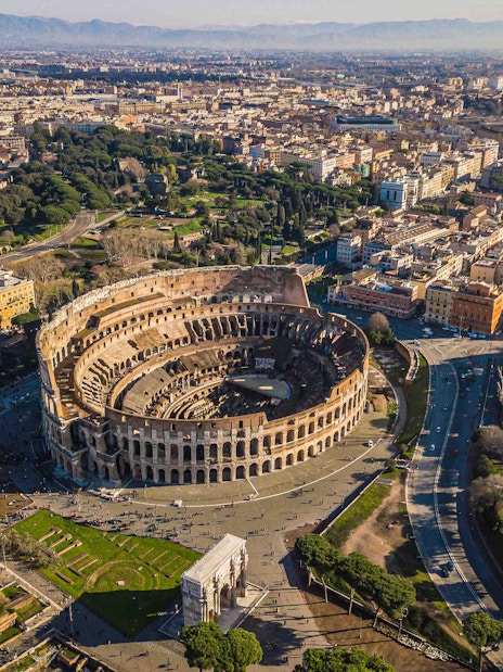 Aerial view of the Colosseum in Rome, Italy, surrounded by cityscape and roads.